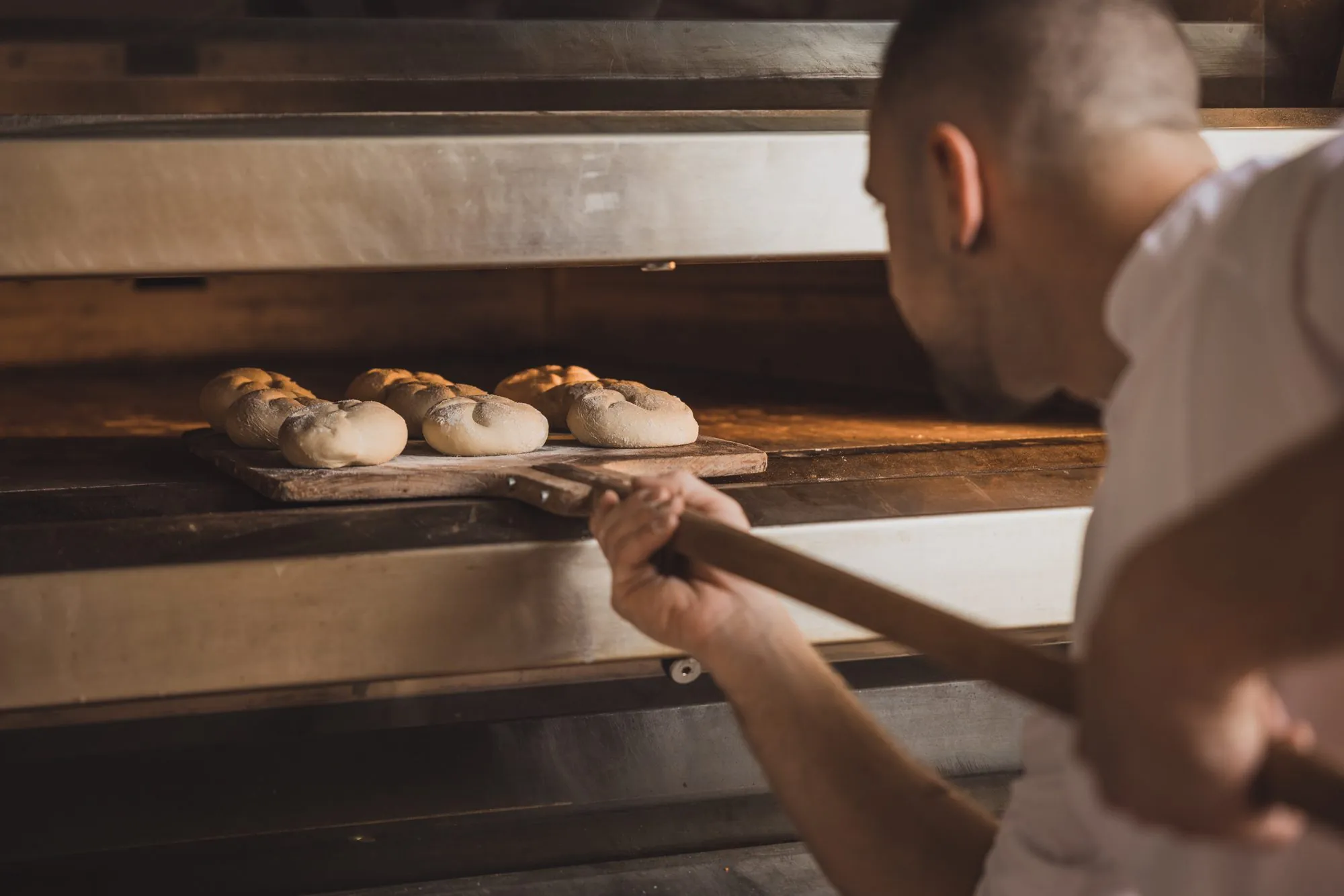 Bäcker schiebt Brotlaibe in den Steinofen, Brotschmiede
