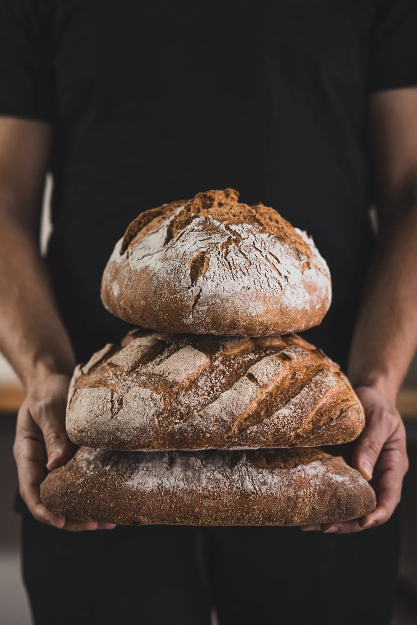 Bäcker hält einen Stapel frischer Brotlaibe, Brotschmiede
