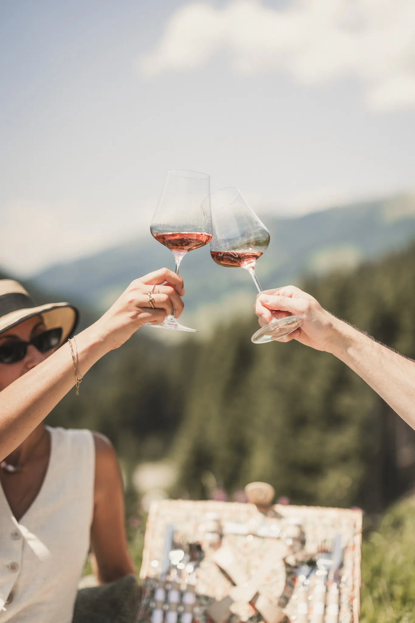 Paar stößt beim Picknick mit Rosé an, Berge im Hintergrund