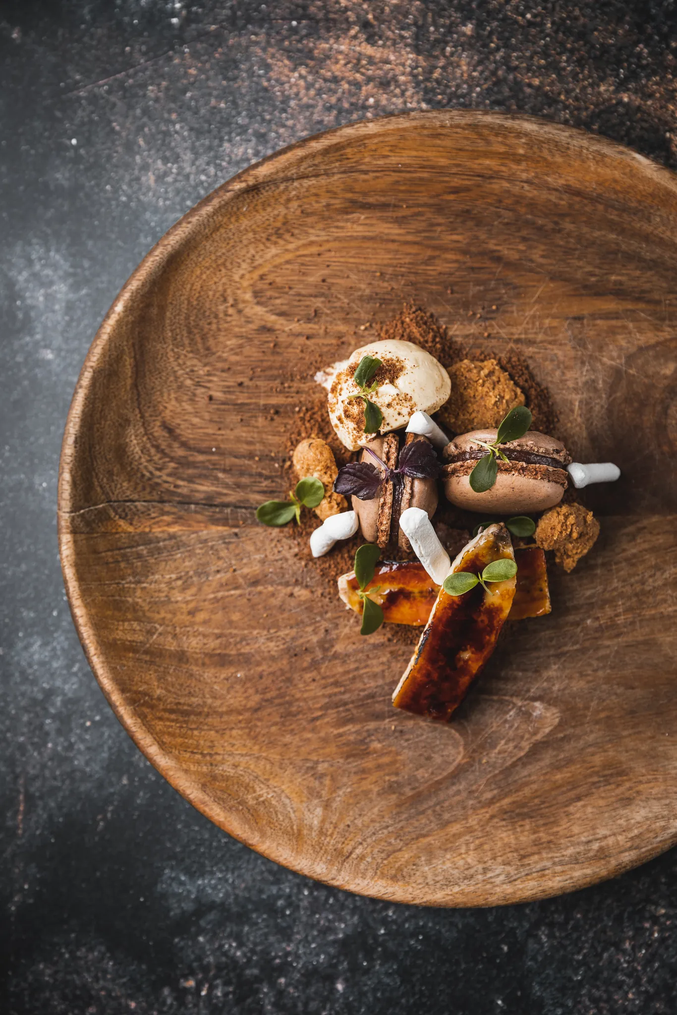 Dessert mit Macarons, karamellisierter Banane und Kakao-Crumble auf Holzteller von oben, Restaurant 23 Reasons