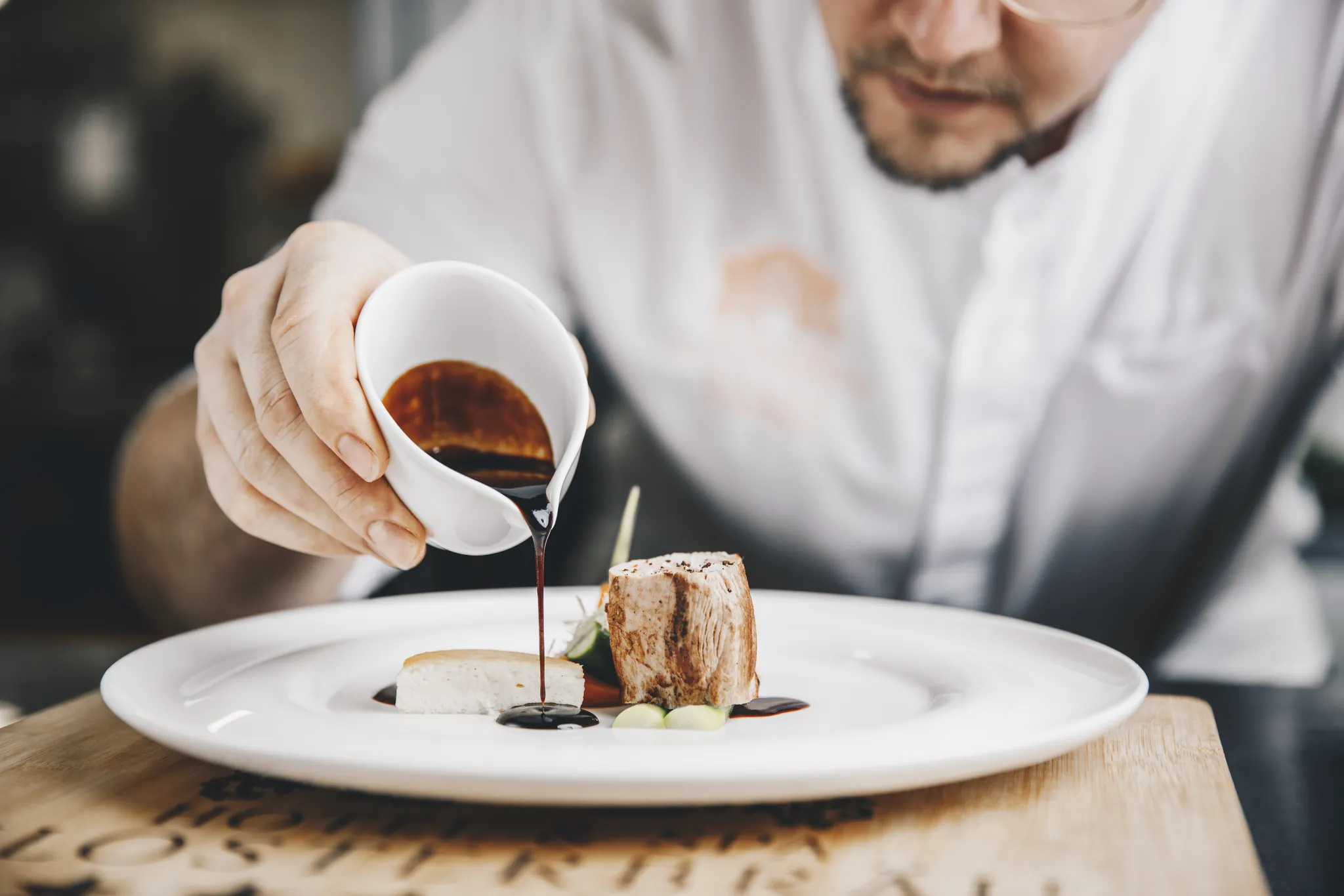 Koch gießt Sauce auf ein angerichtetes Fleischgericht, Hotel Klosterbräu