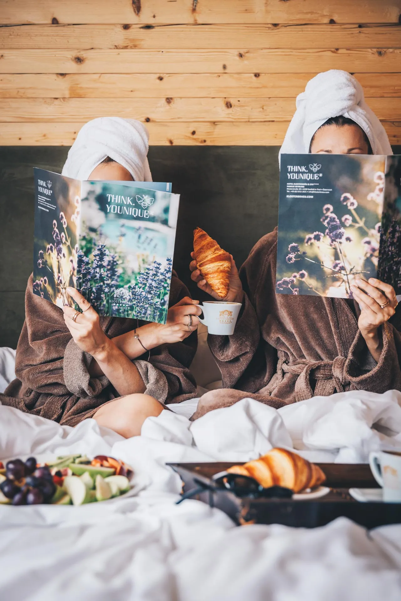 Zwei Freundinnen im Bademantel frühstücken im Bett und lesen das Hotelmagazin, Hotel Klosterbräu