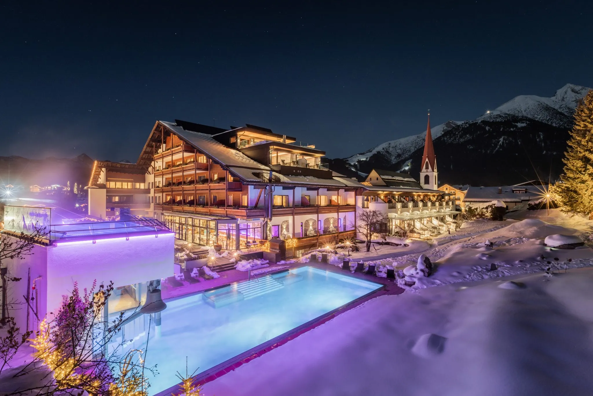 Beleuchteter Außenpool des Hotel Klosterbräu in einer Winternacht, verschneite Berge