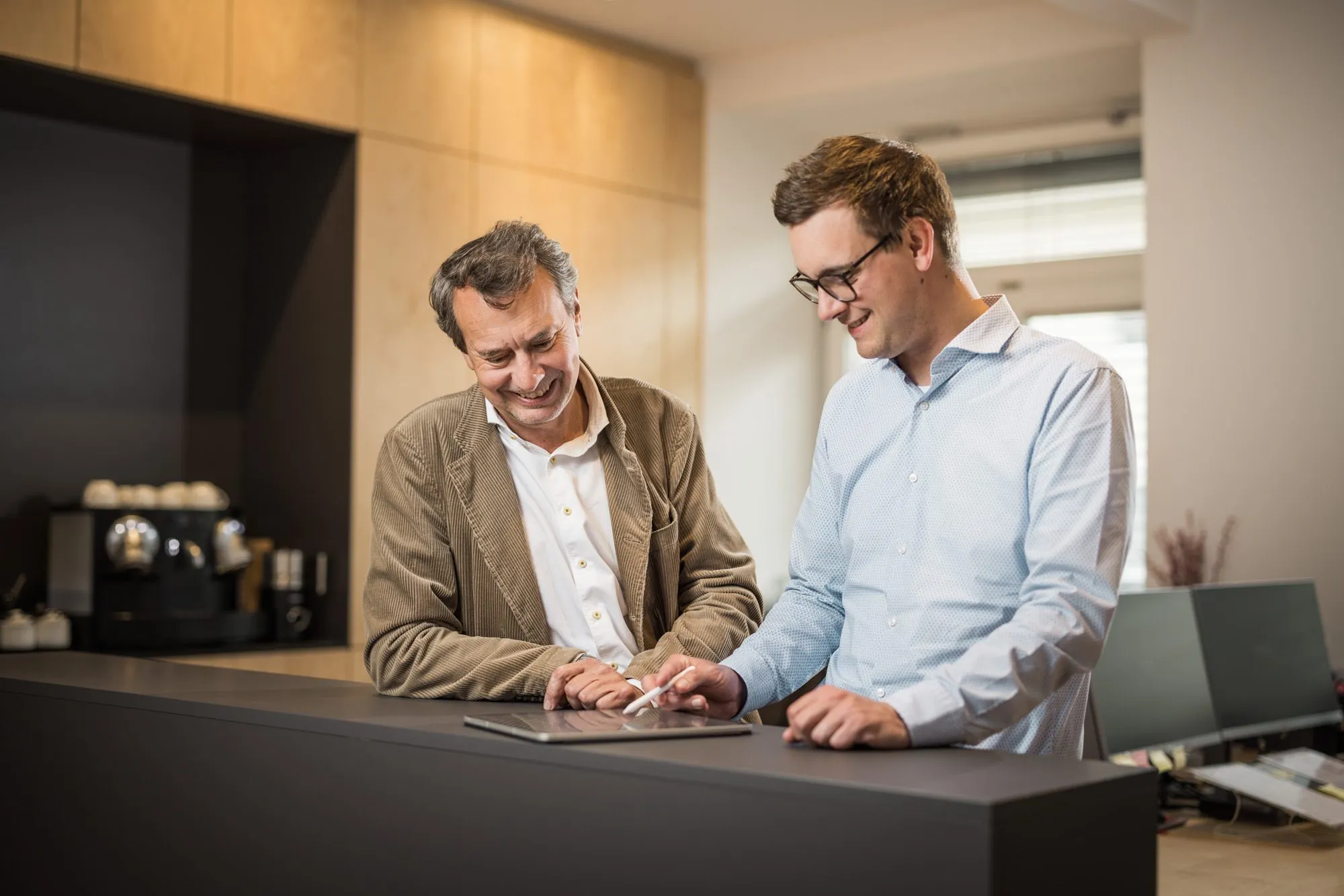 Partner und Mitarbeiter besprechen sich lachend am Tablet