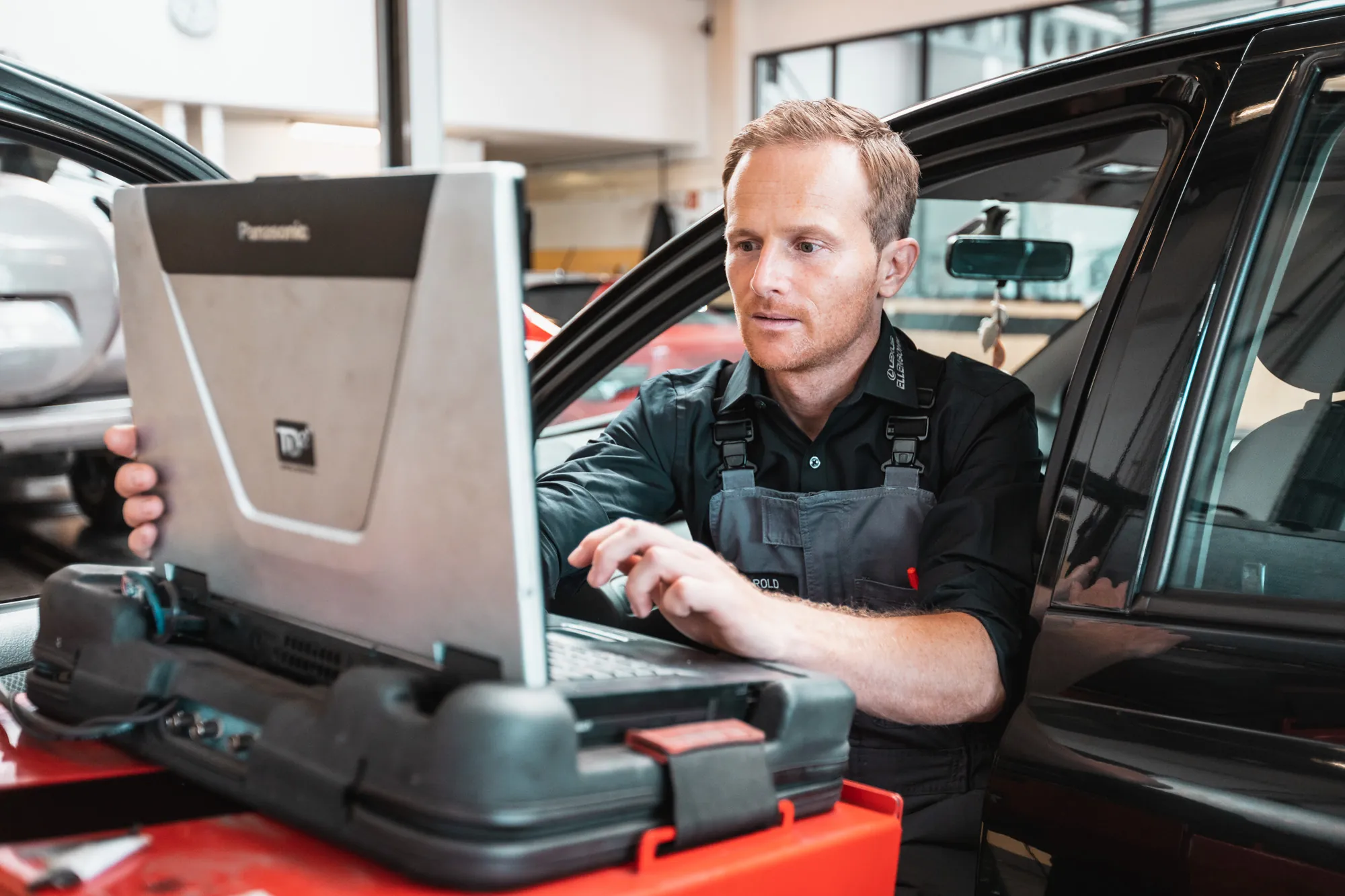 Kfz-Techniker mit Diagnosegerät am Fahrzeug, Mitarbeiterportrait in der Werkstatt