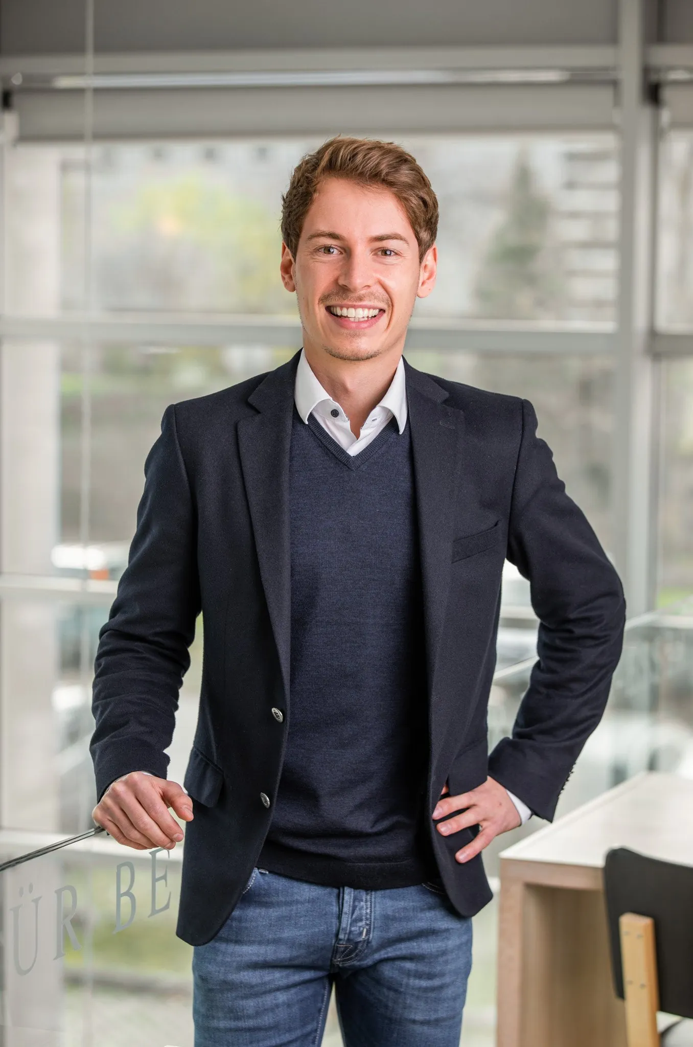 Junger Mitarbeiter im Sakko am Fenster des Büros, Mitarbeiterportrait