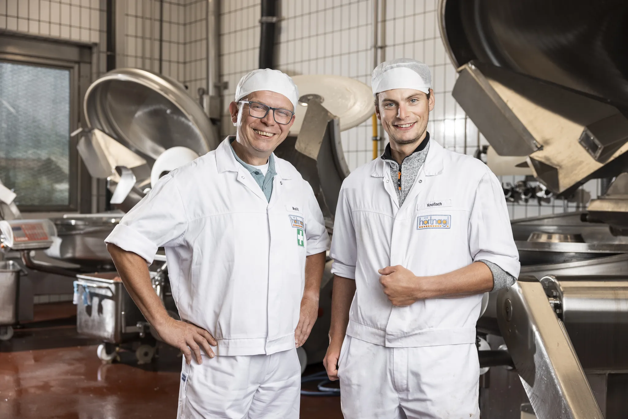 Zwei lachende Mitarbeiter in weißer Arbeitskleidung in der Produktion von Hörtnagl