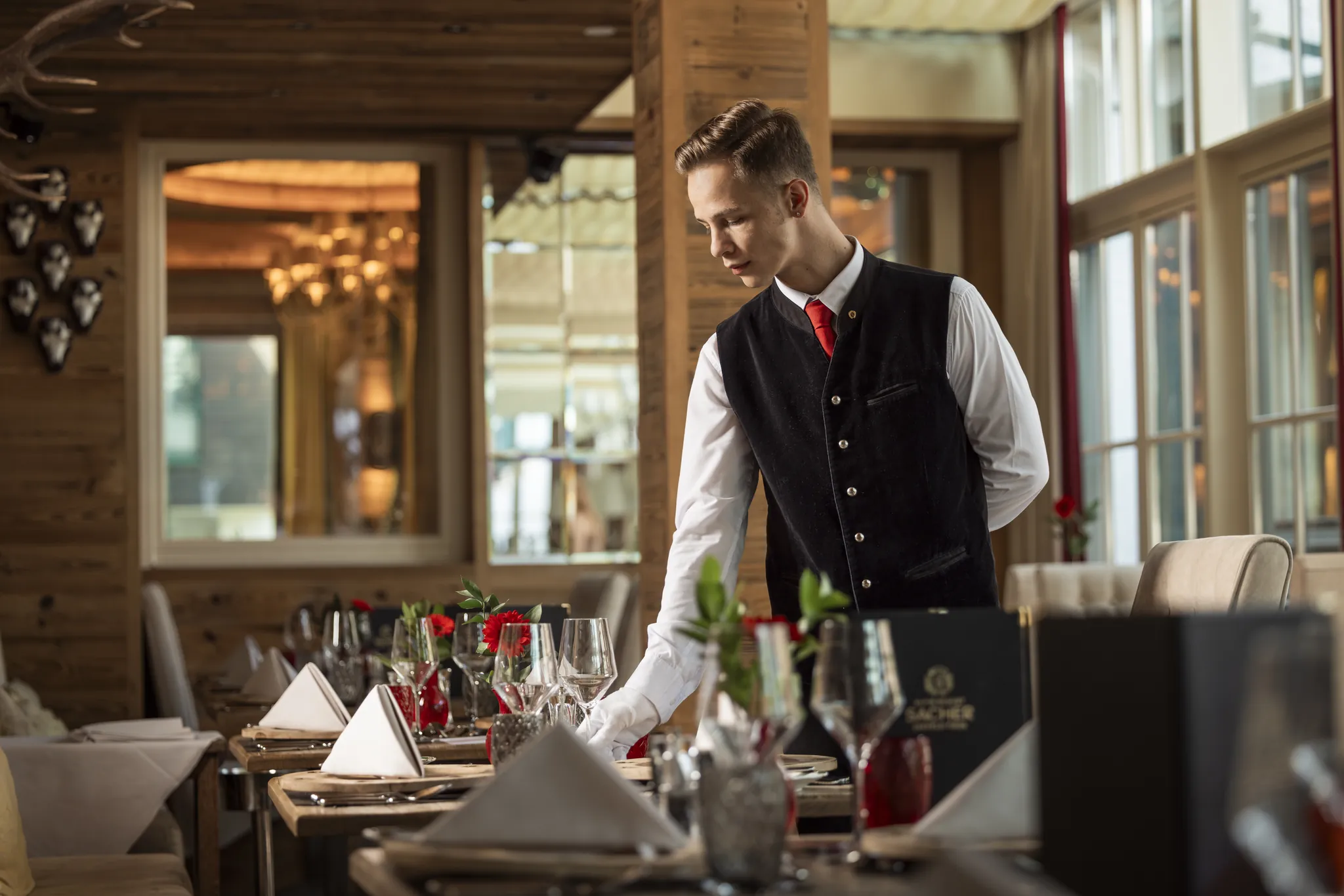 Kellner in Tracht deckt im Restaurant des Alpin Resort Sacher ein