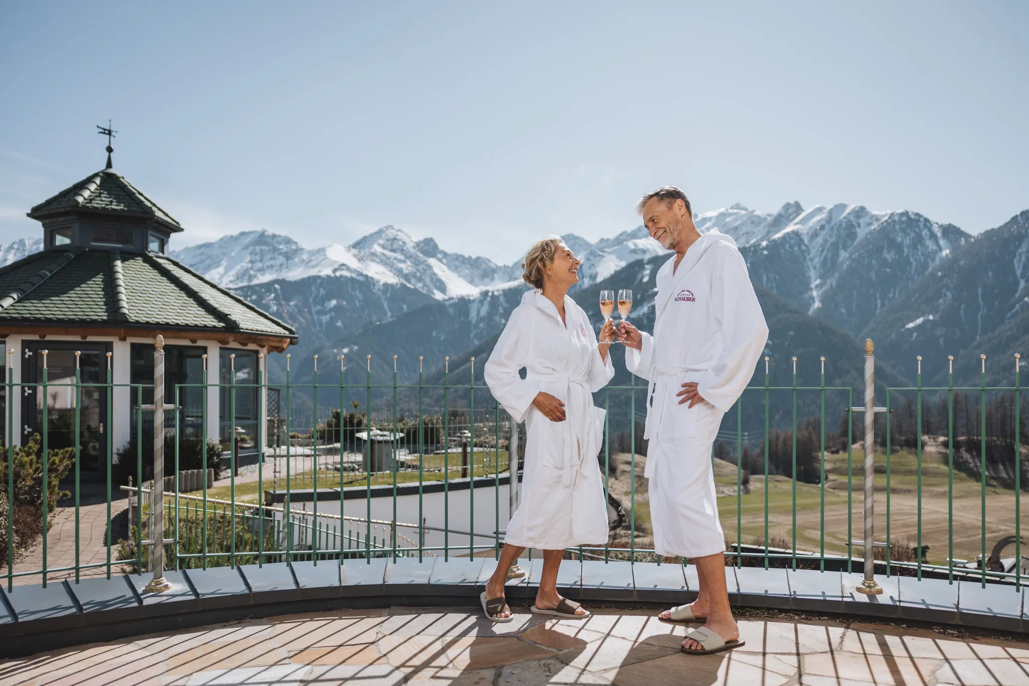 Paar stößt mit Prosecco auf der Terrasse an, Panoramablick auf die verschneiten Berge, Wellnessresidenz Schalber