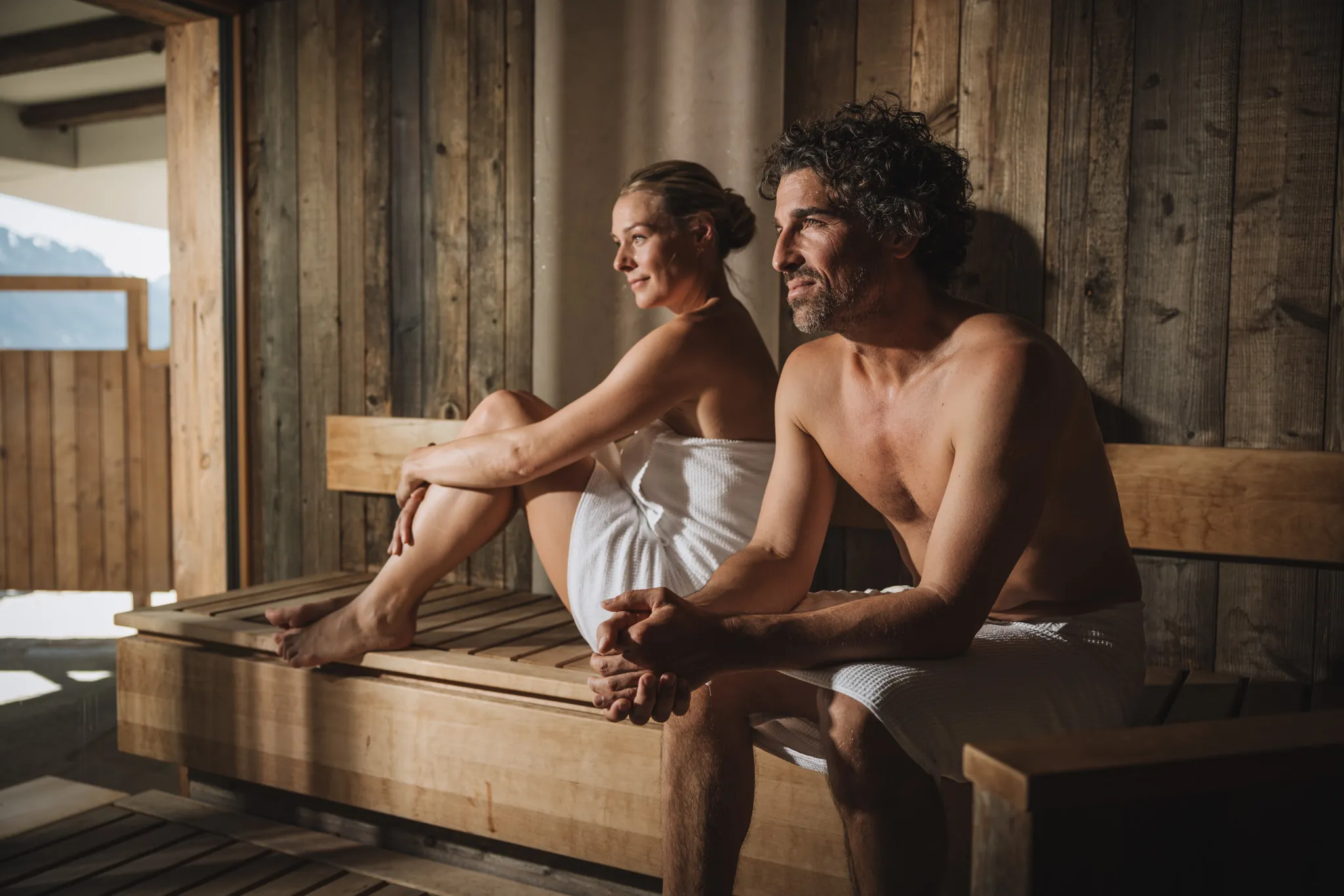 Paar in der Sauna mit Blick durchs Fenster auf die Berge, Wellnessresidenz Schalber