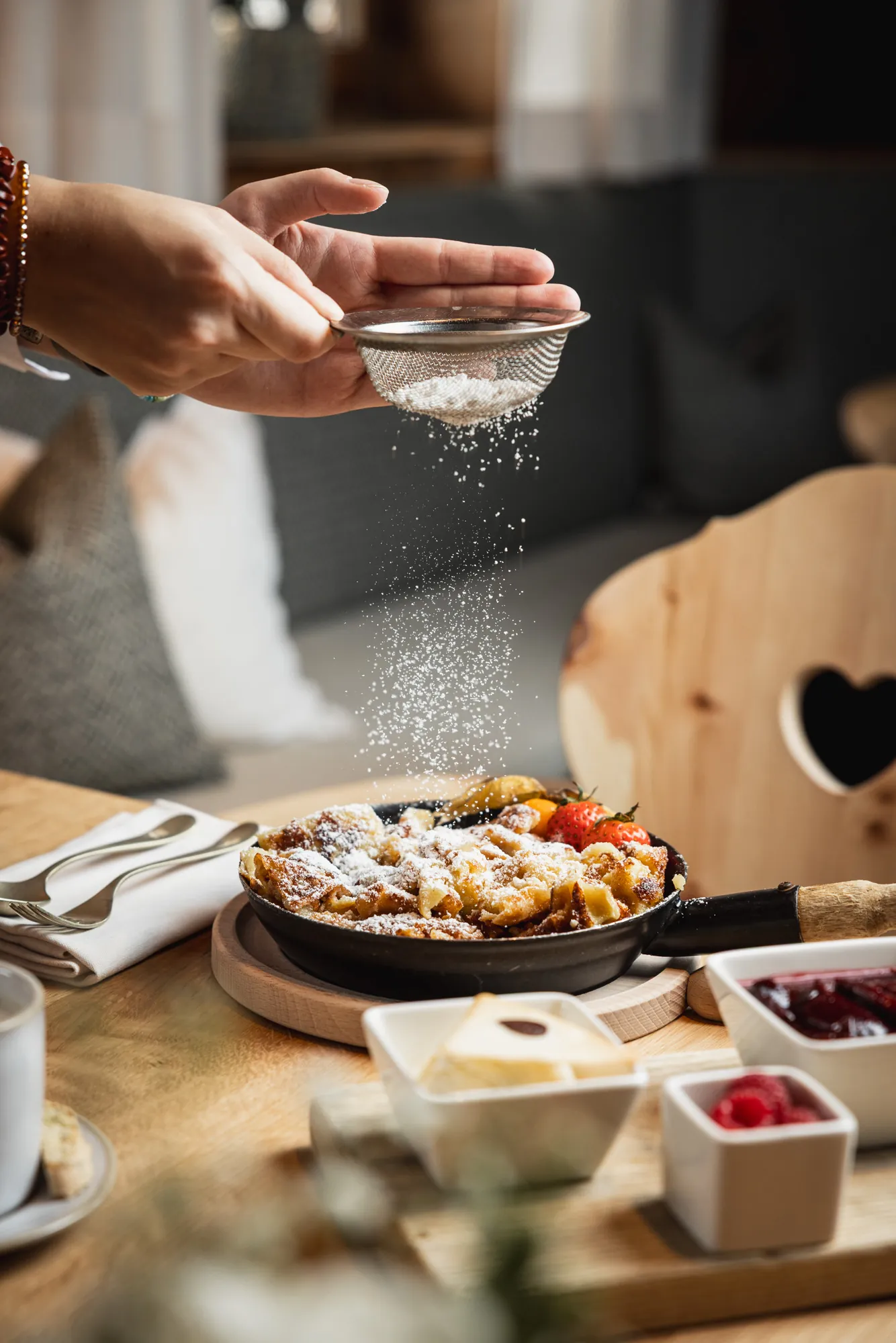 Kaiserschmarrn wird mit Staubzucker bestäubt, gemütliche Stube im Hintergrund
