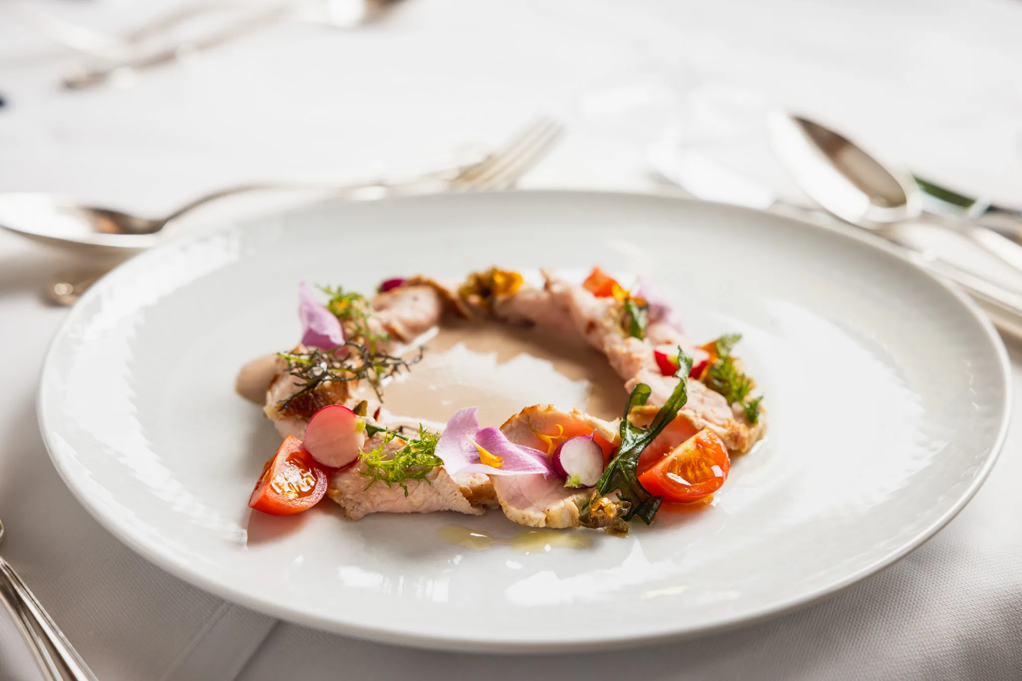 Angerichtetes Kalbsgericht mit Kirschtomaten und essbaren Blüten